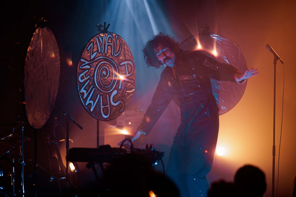 Ziyad Al-Samman en concert, présent au centre de l'image, habillé d'une combinaison noire. En arrière-plan, une gross cymbale avec son nom inscrit dessus.